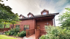 A log cabin with a wooden deck, a front porch, and a small garden area. - Luxurious Walk-in Cabin with Private Screened Deck in the Heart of Branson (Branson)