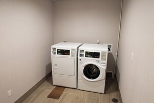 Un área de lavandería con dos electrodomésticos apilados, una secadora y una lavadora, ubicada en un rincón con piso de cerámica.
