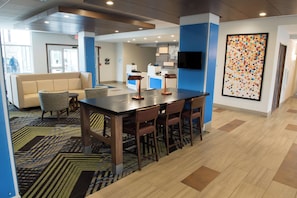 A modern hotel lobby with a reception desk, seating area, and a large colorful artwork. - Holiday Inn Express & Suites Louisville N - Jeffersonville by IHG (Jeffersonville)