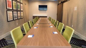 Ein Konferenzraum mit einem langen Tisch, grünen Stühlen und gerahmten Kunstwerken an den Wänden.
