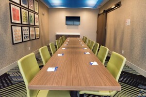Un salón de conferencias con una larga mesa, sillas verdes y obras de arte enmarcadas en las paredes.