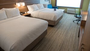 Une chambre d’hôtel avec deux lits, un bureau, une chaise et une grande fenêtre.
