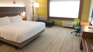 Ein Hotelzimmer mit einem großen Bett, einem Schreibtisch mit Stuhl, einer kleinen Sitzecke, einem Fenster und einer Klimaanlage.