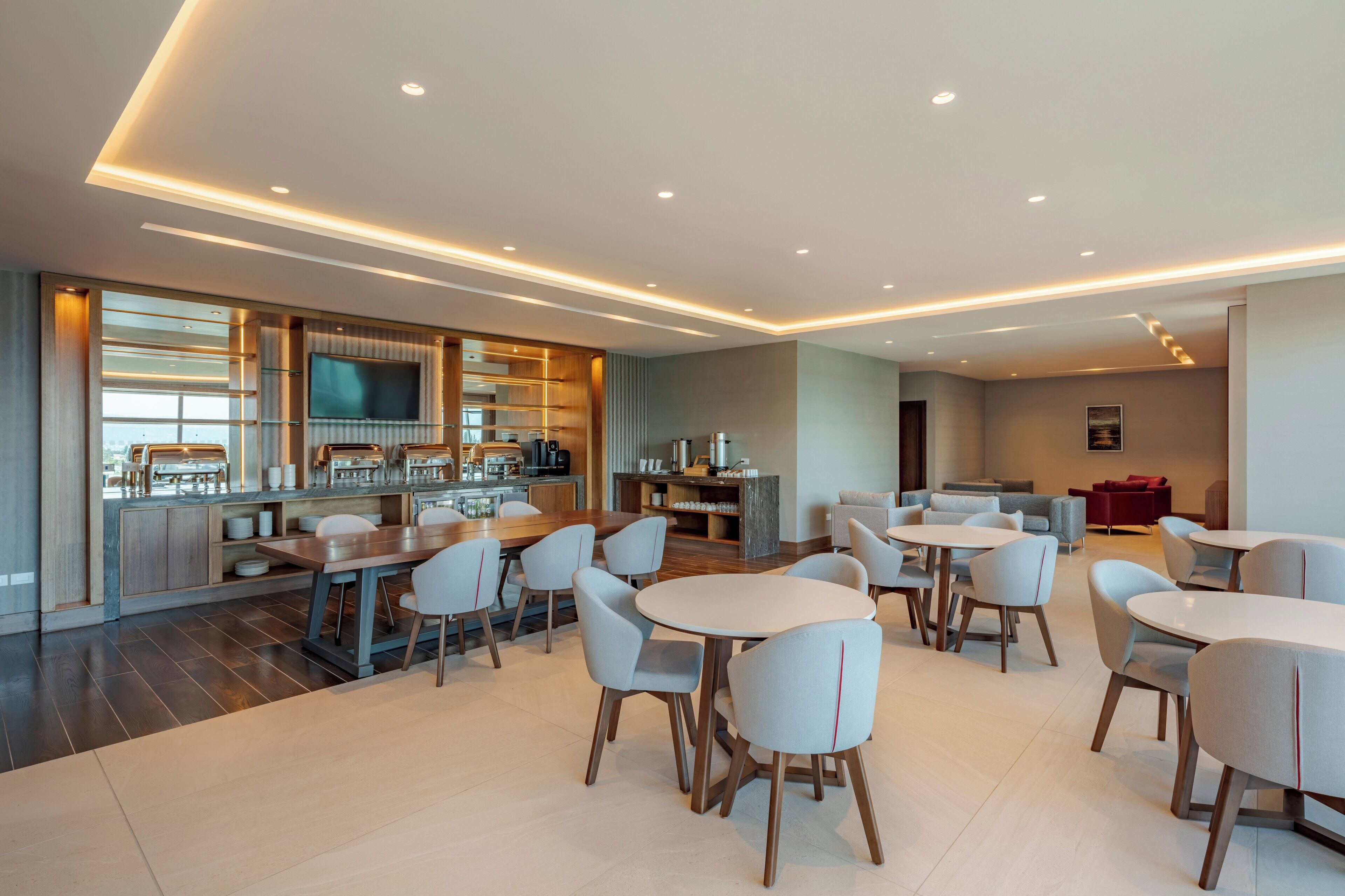Un hall d’hôtel moderne doté d’un bar, de différents espaces aménagés pour s’asseoir et d’un grand téléviseur à écran plat.