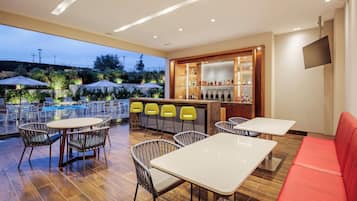 Un espacio al aire libre con mesas, sillas, una piscina y un bar con botellas.