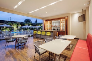 Espaço ao ar livre com mesas, cadeiras, piscina e bar com garrafas.