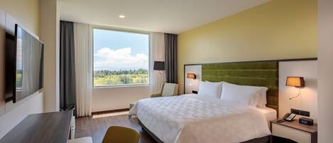 Habitación de hotel con cama, escritorio, silla, televisor y ventana con vista al exterior.