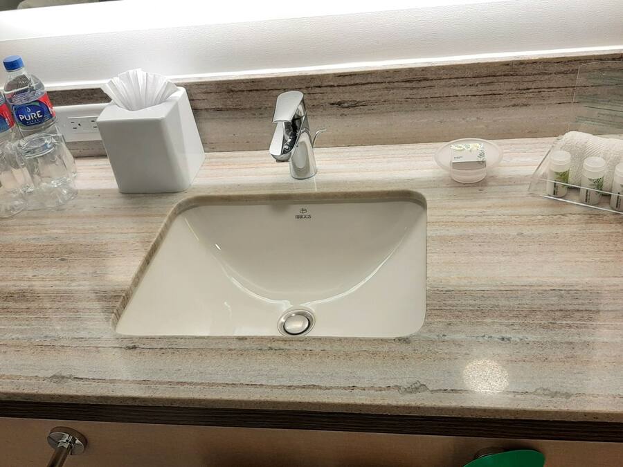 A bathroom sink with a marble countertop, a white soap dispenser, a tissue box, and a bottle of water.