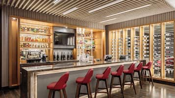 A bar area with a long counter, multiple shelves of bottles, and a large TV screen.