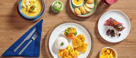 Una mesa de madera con diversos platos que incluyen sopa, arroz, camarones y plátanos.