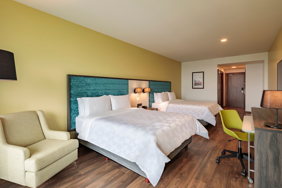 Ein Hotelzimmer mit zwei Betten, einem Schreibtisch, einem Stuhl und einem Sofa.