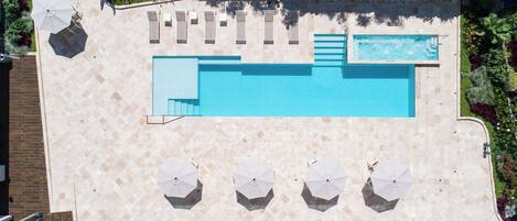 An aerial view of a swimming pool area with a tiled deck, lounge chairs, and umbrellas.
