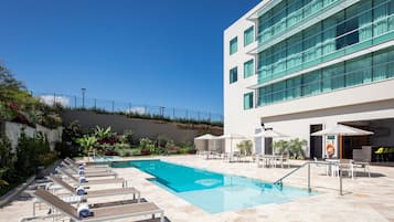 Una piscina al aire libre, sombrillas, sillones reclinables de piscina