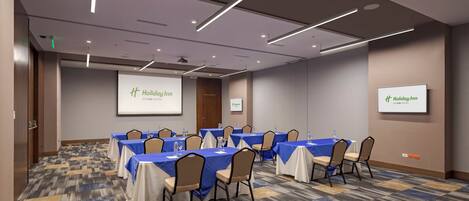 Un salón de conferencias con varias mesas, sillas y una pantalla de proyecciones.