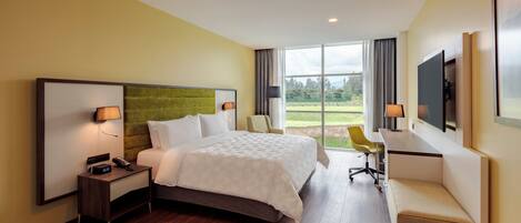 A hotel room with a large bed, a desk, a chair, and a TV.