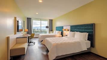 A hotel room with two beds, a desk, a chair, and a view of the outdoors.