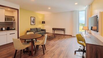 Habitación de hotel moderna con comedor, sofá, televisión de pantalla plana y vistas al exterior.