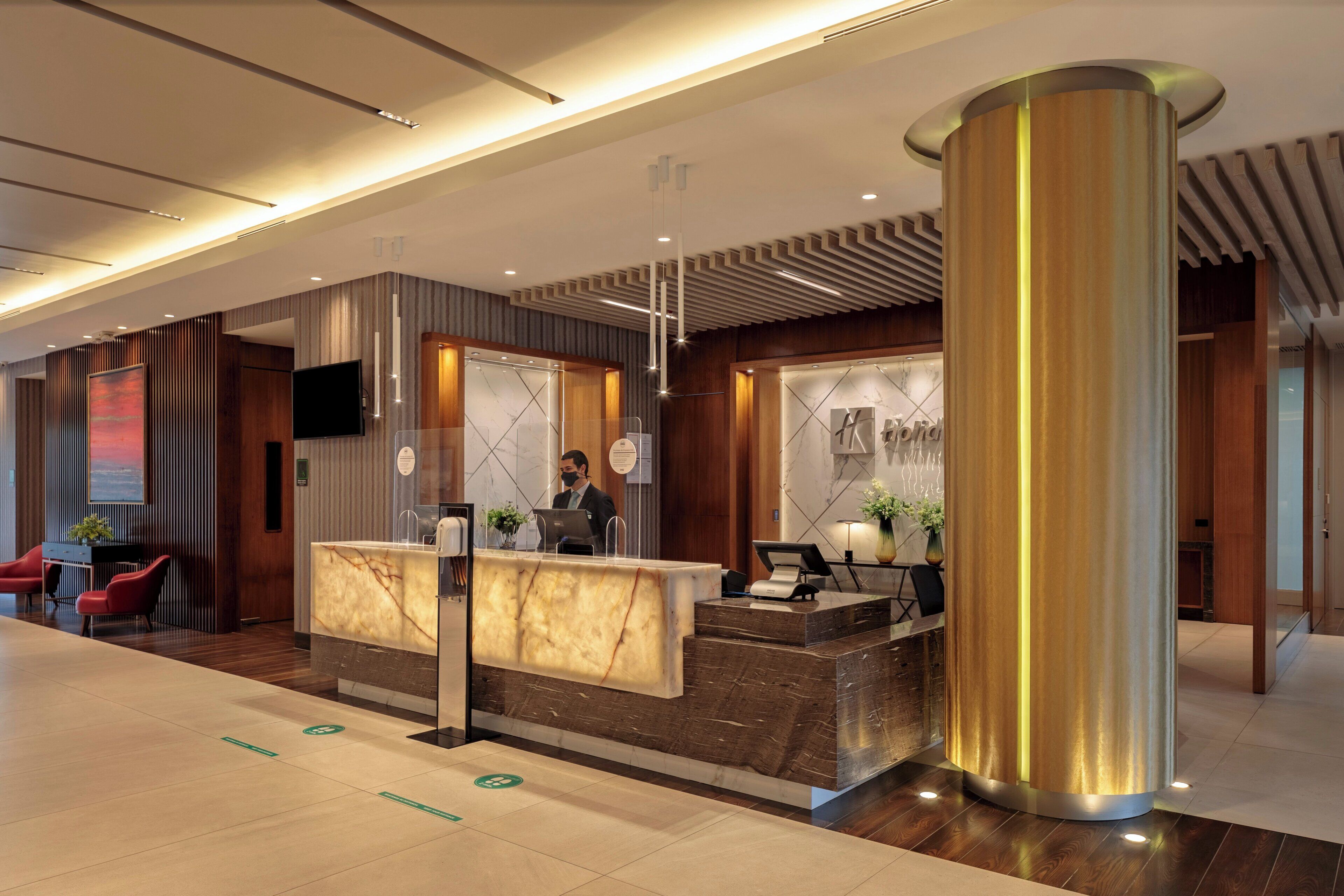 A hotel reception area with a marble counter, a large pillar, and a modern ceiling design.