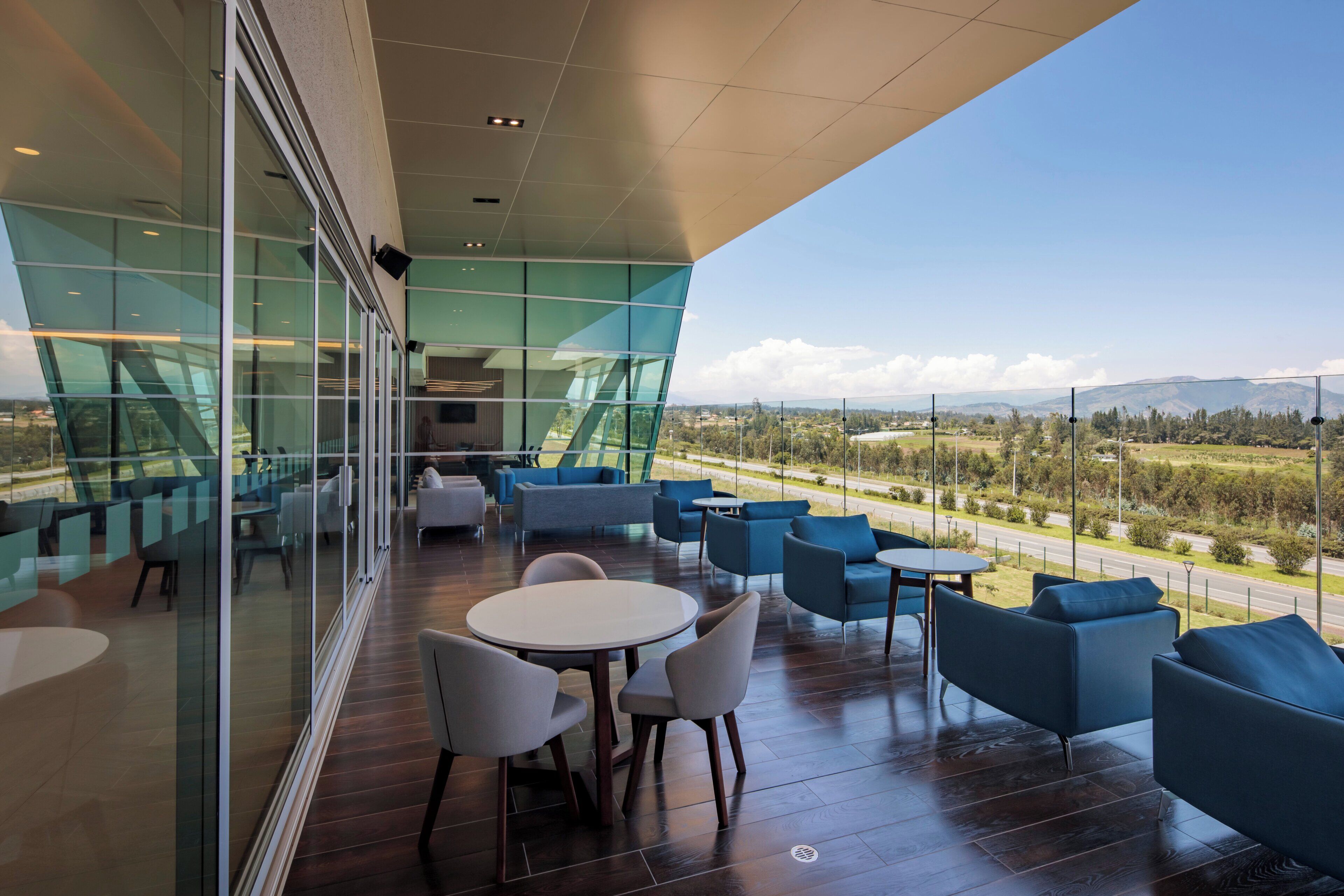 A modern outdoor seating area with glass walls, offering a view of a road and distant mountains.
