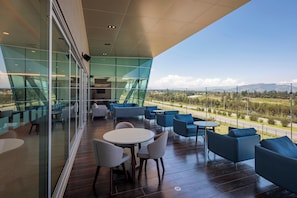 Un espacio moderno para sentarse al aire libre con paredes de vidrio, con vistas a una carretera y montañas distantes.