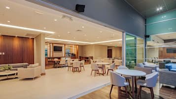 Un moderno vestíbulo de hotel con zona de comedor, sofás y una cocina visible a través del muro de vidrio.