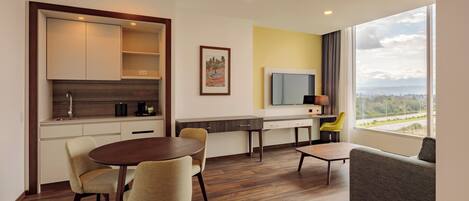 A modern kitchen with a dining area, a sofa, and a large window offering a view.