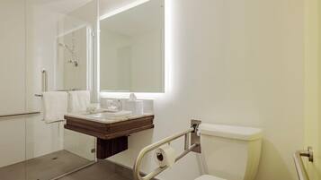 A modern bathroom with a glass shower enclosure, a vanity with a mirror, and a toilet with a grab bar.
