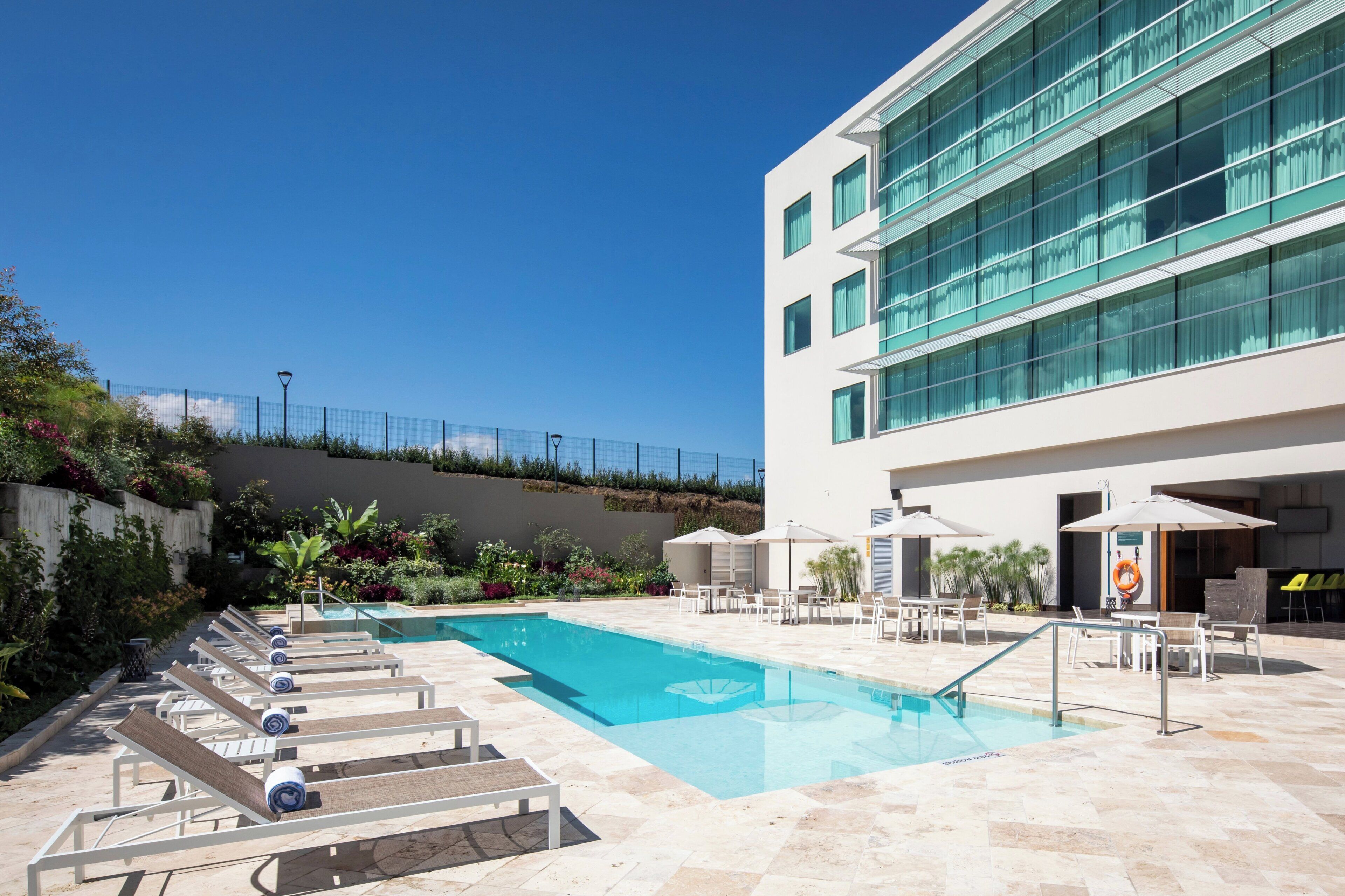A modern hotel with a swimming pool, outdoor seating, and a building with large windows.