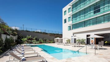 A modern hotel with a swimming pool, outdoor seating, and a building with large windows.