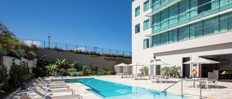 A modern hotel with a swimming pool, outdoor seating, and a building with large windows.