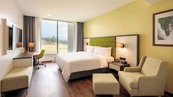 A hotel room with a bed, desk, chair, and a view of the outdoors.