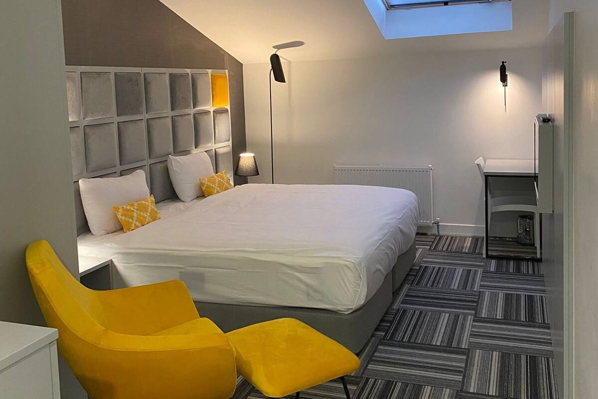 A modern hotel room with a large bed, a skylight, a desk, and a chair.