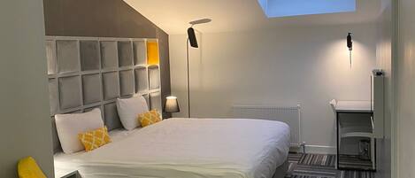 Una habitación de hotel moderna con una cama grande, tragaluz, escritorio y una silla.
