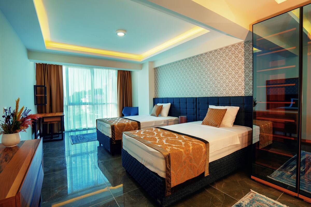 A hotel room with two beds, a desk, a chair, and a large window with curtains.