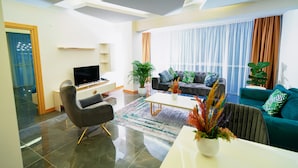 A modern living room with a flat-screen TV, a sofa, a coffee table, and a dining area.