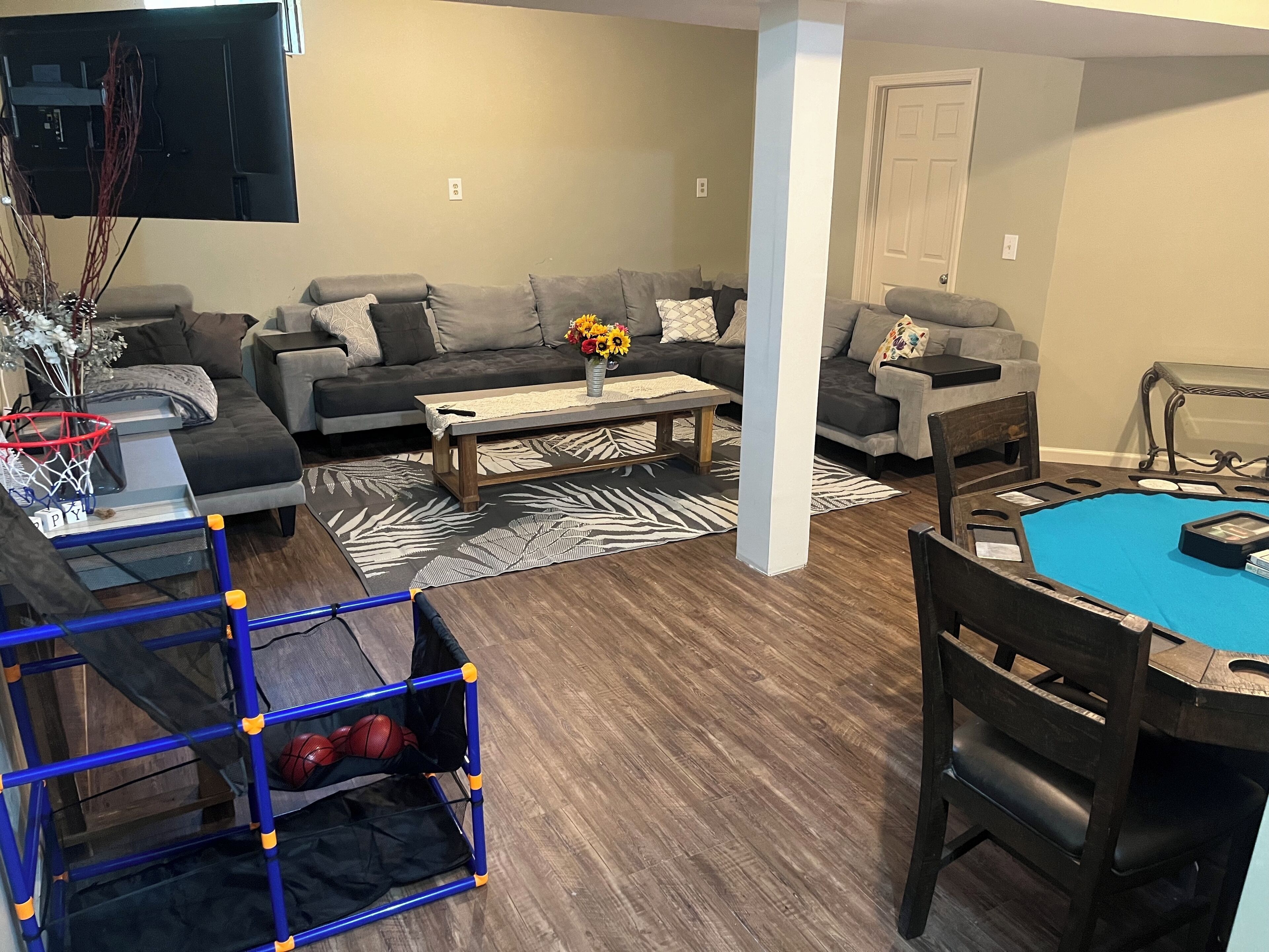 A living room with a grey sofa set, a coffee table, a blue playpen, and a dining table with chairs.