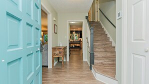 A hallway with a wooden staircase, a blue door, and a kitchen area in the background. - Family Launch Pad (Asheville)