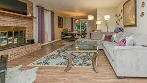 A living room with a fireplace, a glass coffee table, a sofa, and a dining area. - Family Launch Pad (Asheville)