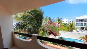 Un balcón con vistas a una piscina, palmeras y un edificio moderno.