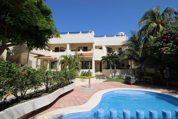 A hotel with a swimming pool, palm trees, and a clear blue sky.