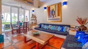 Un espacio habitable amplio con una mesa de centro de madera, un sofá azul oscuro con cojines estampados y un cuadro grande sobre el sofá.