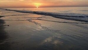 A beach at sunset with calm waves and a clear sky.