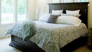 Un dormitorio con una cama grande, un ventilador de techo y tres ventanas.