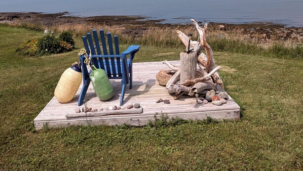 A picnic setup with a blue chair, a green ball, and a log on a grassy area near a body of water. - Fundy Sunset Cottage, Oceanfront Tranquility!! (granville ferry)
