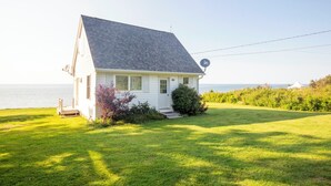 A white house with a grey roof, a satellite dish, and a grassy lawn. - Fundy Sunset Cottage, Oceanfront Tranquility!! (granville ferry)