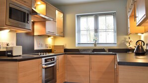 A modern kitchen with wooden cabinets, stainless steel appliances, a built-in oven, and a window with blinds. - 2 bedroom accommodation in Filey (Filey)