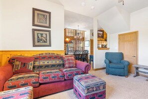 A cozy living room with a red sofa and ottoman, a blue armchair, and a wooden bench.