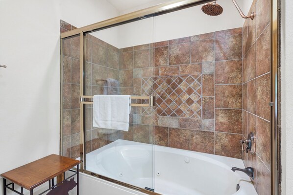 A glass-enclosed shower area with a white bathtub, tiled walls, and a wooden bench.