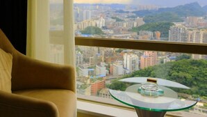 A room with a large window offering a cityscape view, a round glass table with a decorative item, and a beige sofa. - Greentree Alliance Hotel Guiyang Huaguo Community Central Business Zone (Guiyang)
