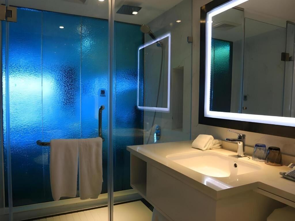 A modern bathroom with a glass shower enclosure, a white sink, and a large mirror.